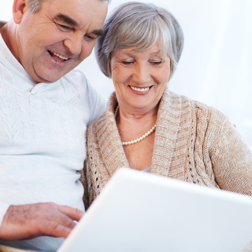 A smiling elderly couple sit together in front of a laptop