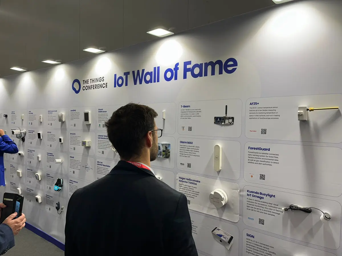 A visitor reads the IoT Wall of Fame of The Things Conference, a long white wall of sensors and trackers, each mounted beside a card describing it