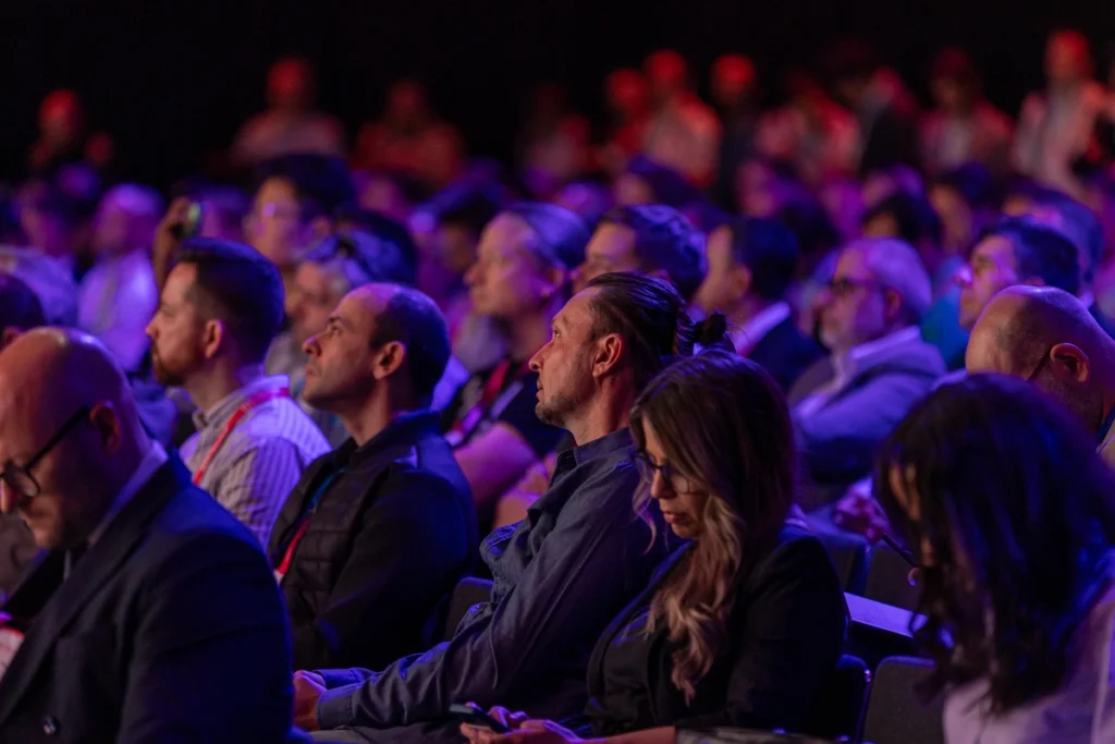 Rows of attendees following a session in a dark auditorium lit in red and violet