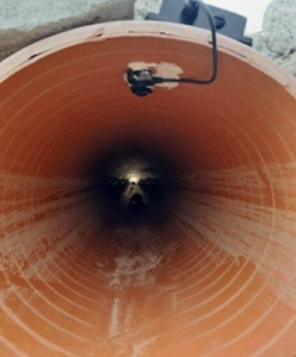 Looking into an orange corrugated pipe from its mouth, with the ultrasonic sensor and its cable fixed to the top of the pipe wall