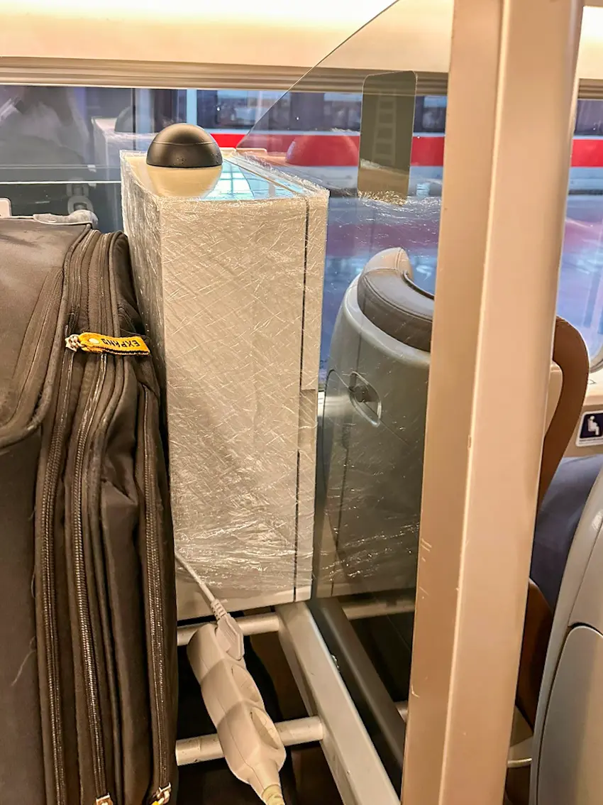 The airCAT edge node, a wrapped enclosure with a dome sensor on top, placed in the luggage rack of a train carriage