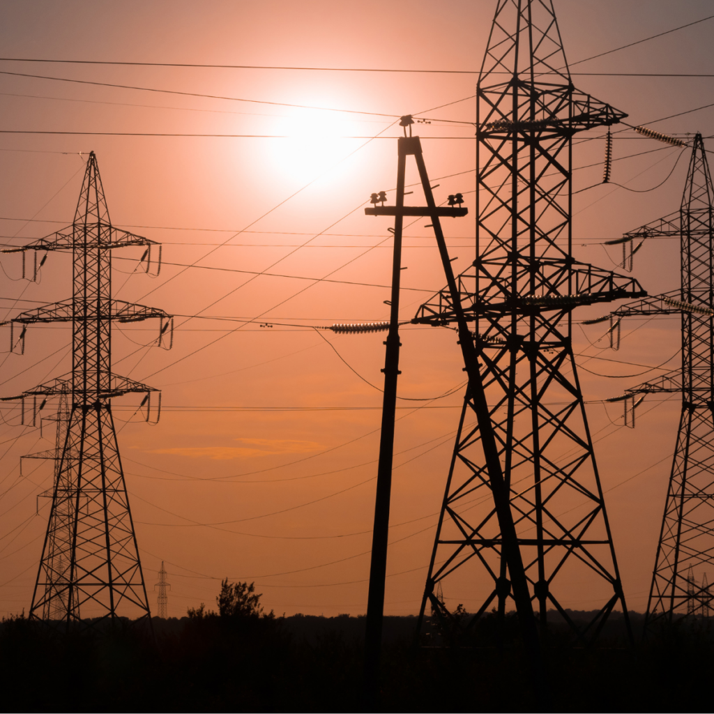 Silhouettes of high-voltage transmission towers and a utility pole against an orange sunset sky